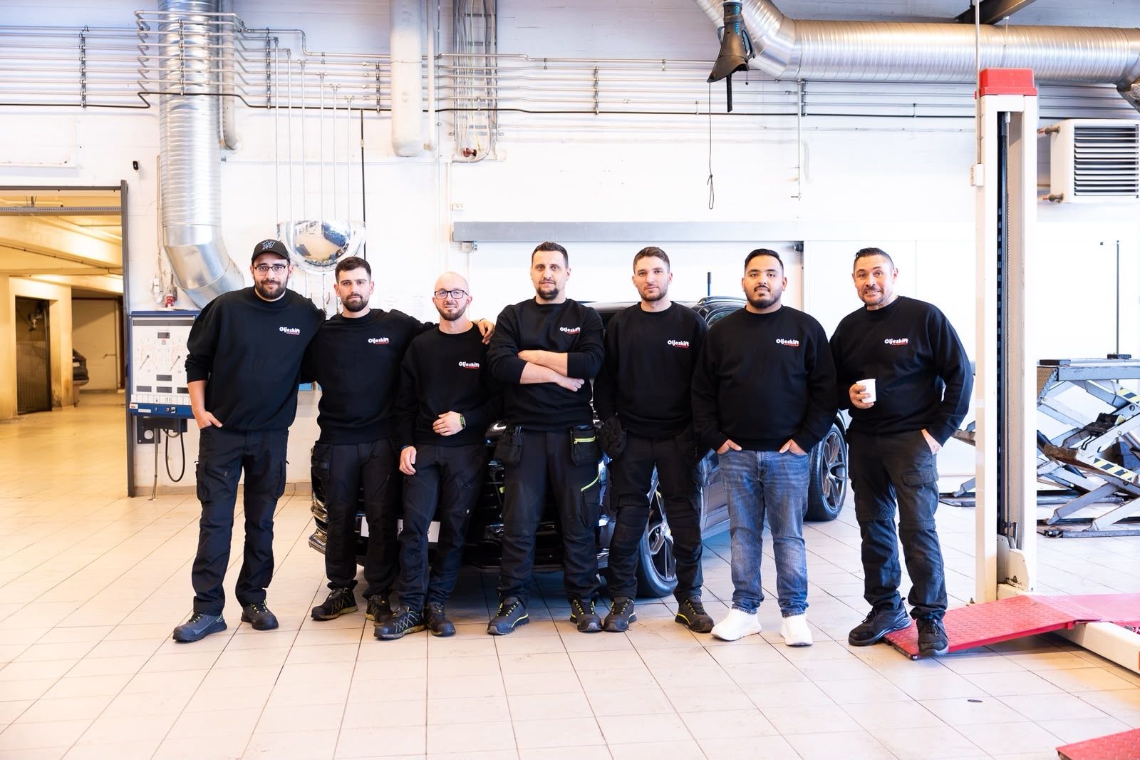 Seven technicians with high-voltage expertise standing in front of a car in the workshop hall