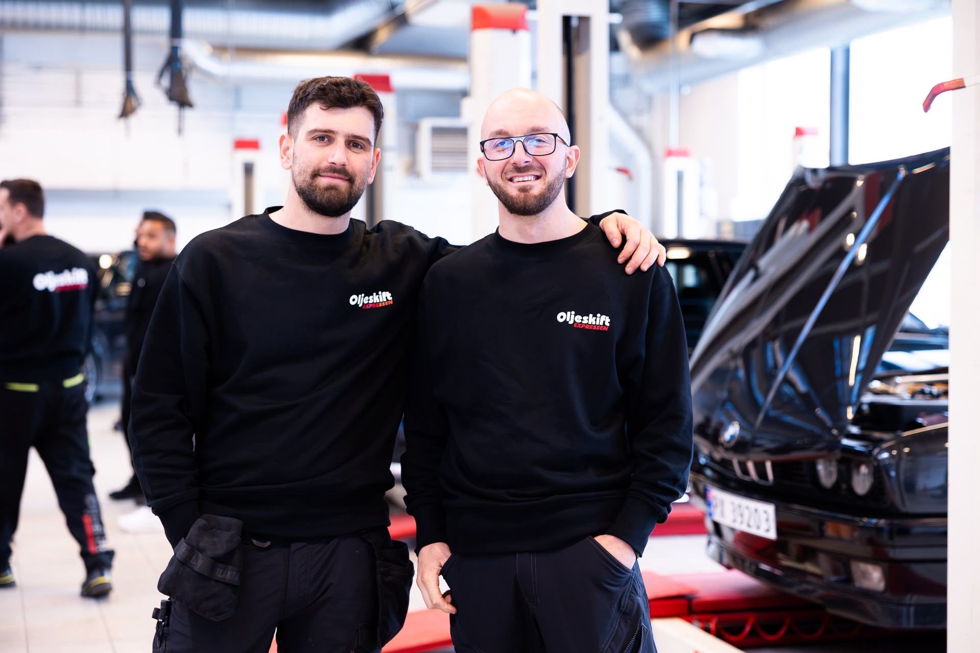 Two smiling technicians in front of a BMW on the lift in the workshop