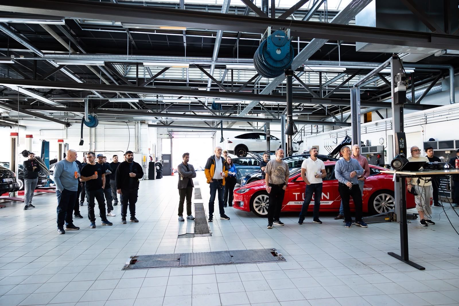 Red TOCN Tesla Model S and white Model S on the lift in the workshop hall